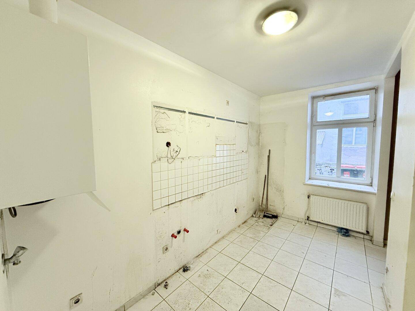 Renovierungsbedürftige Küche mit Fliesenboden, Fenster und Heizkörper, bereit für eine Neugestaltung.