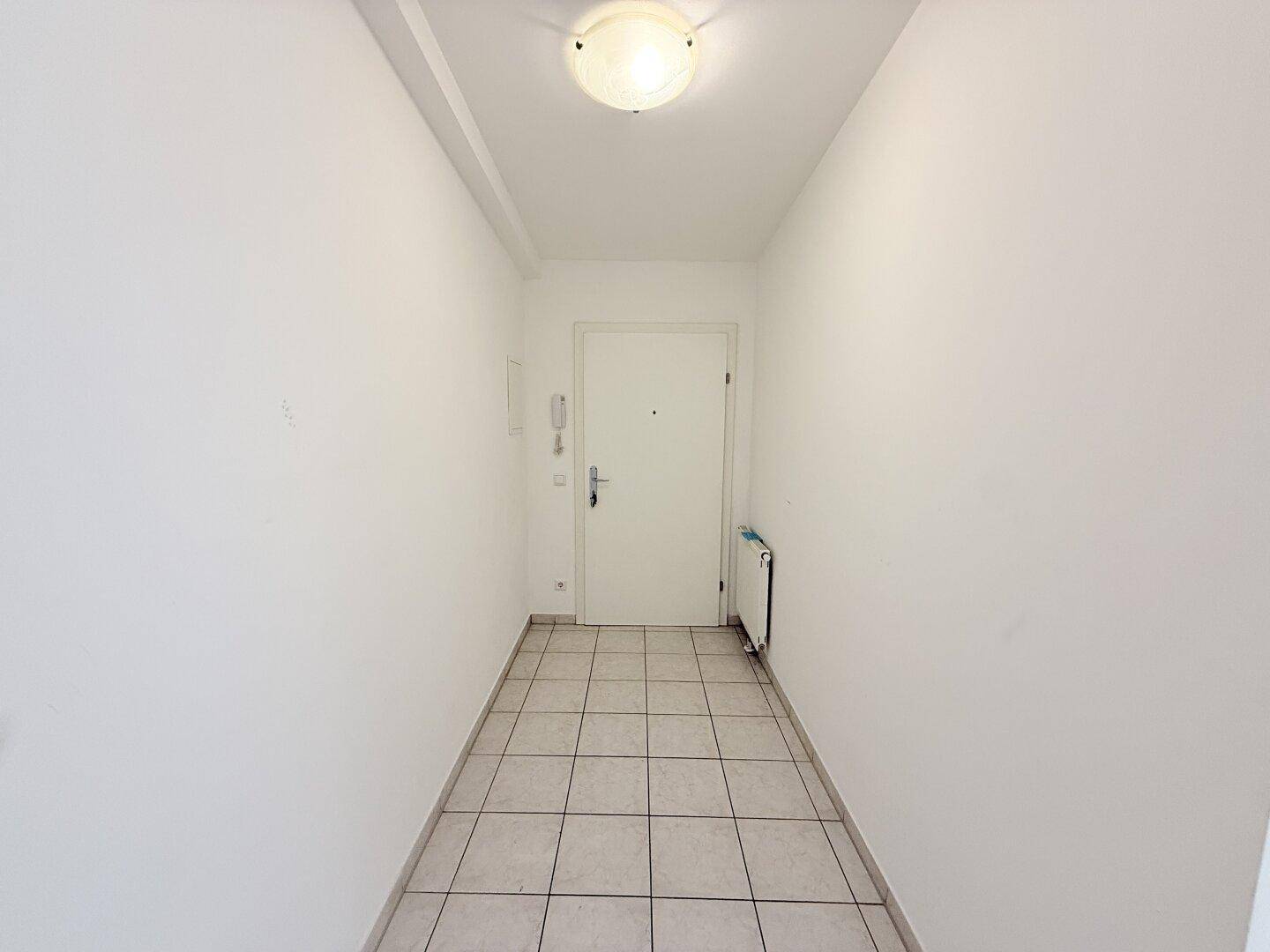 Eingangsbereich mit Fliesenboden, weiß gestrichenen Wänden und Gegensprechanlage.