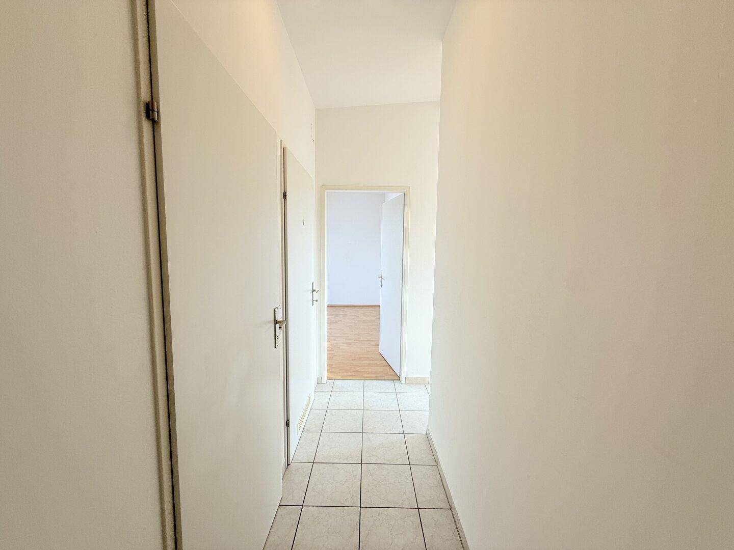 Langer Flur mit hellen Fliesen, der zu weiteren Räumen der Wohnung führt.