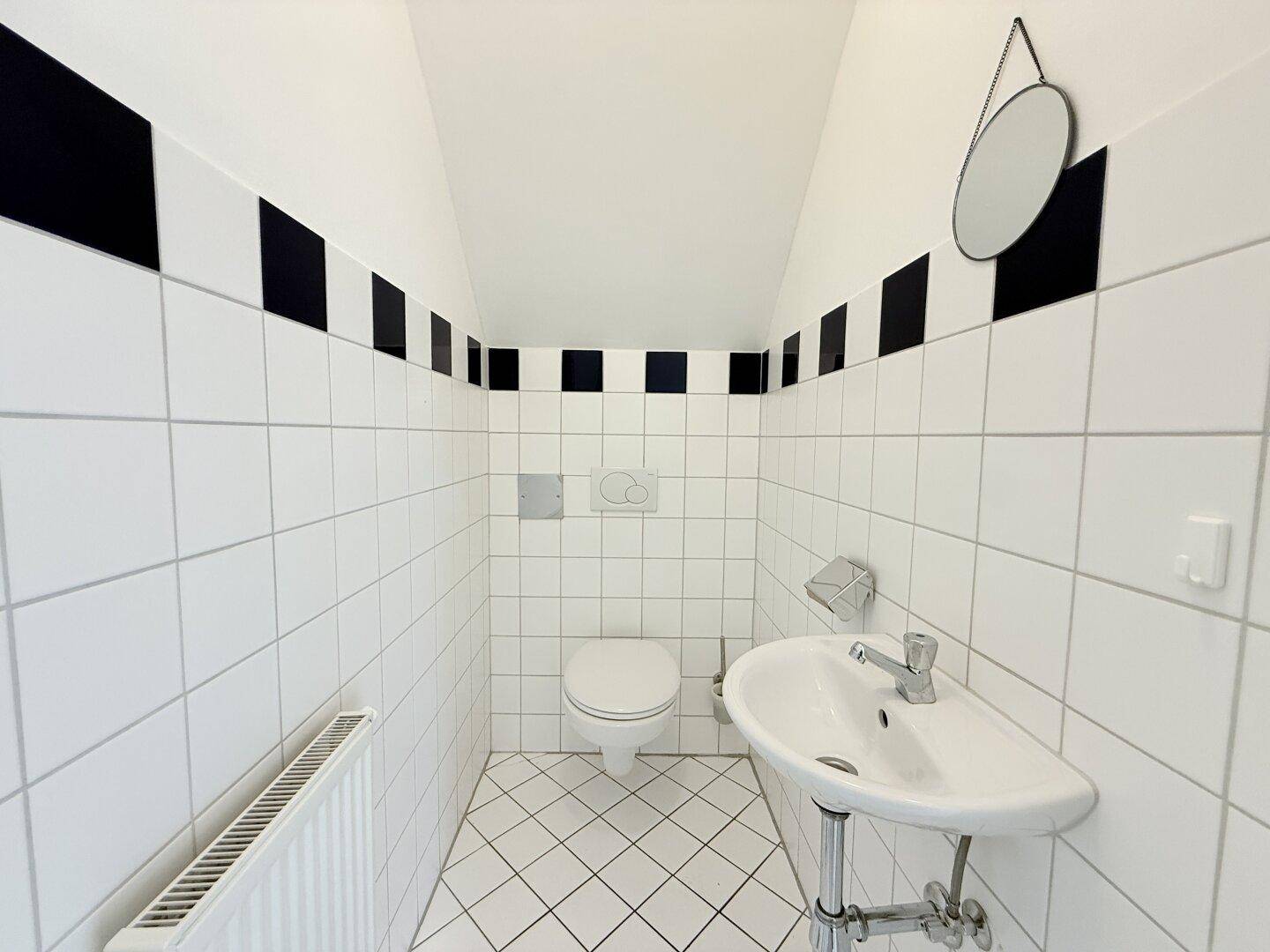 Gäste-WC mit schwarz-weißen Fliesen, wandhängendem WC und Waschbecken.