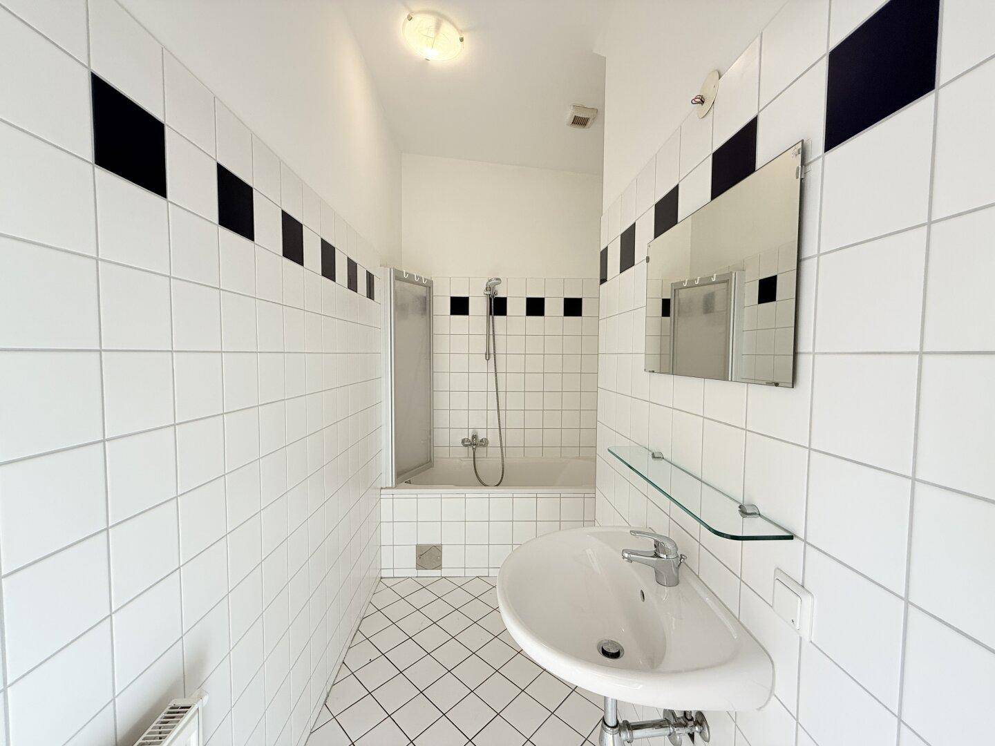 Badezimmer mit Badewanne, Duschabtrennung, Waschbecken und schwarz-weißen Fliesen.