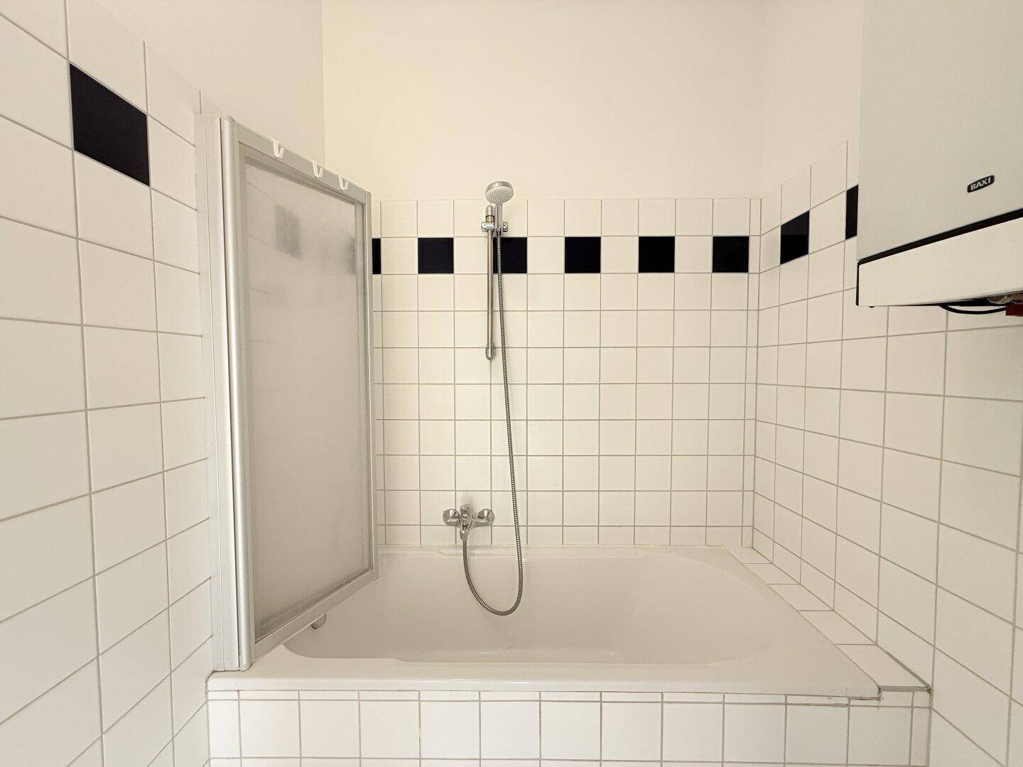 Badewanne mit integrierter Duschfunktion und Duschabtrennung in einem gefliesten Bad.