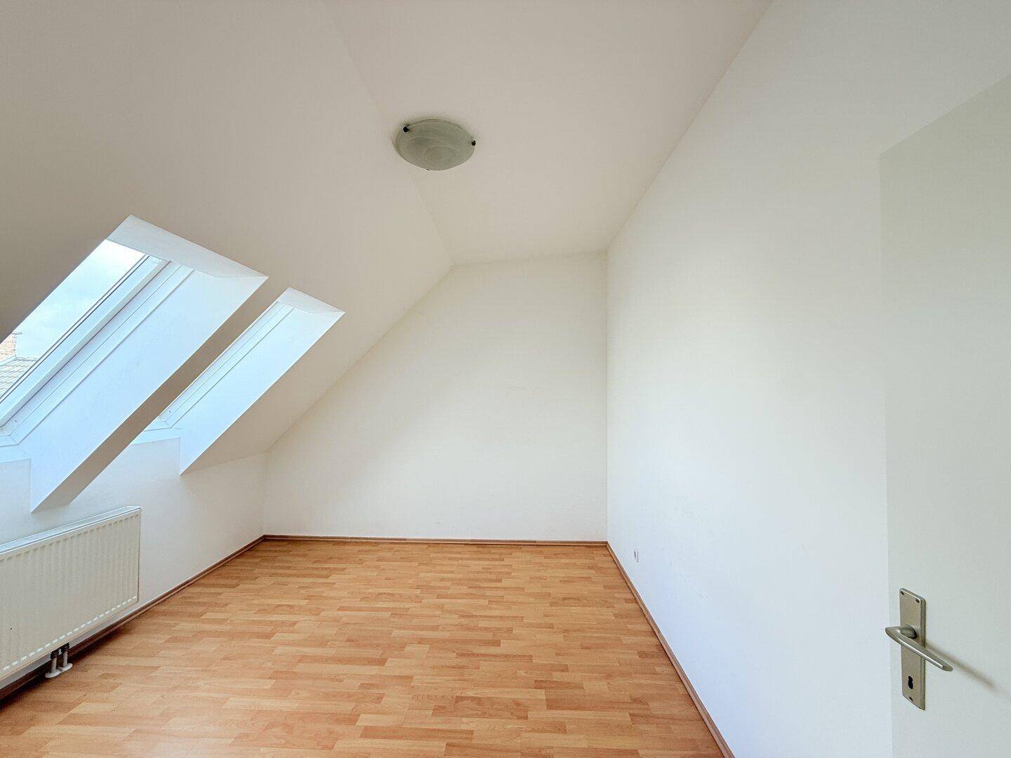 Helles Schlafzimmer mit Dachschrägen, zwei Dachfenstern und Holzboden.