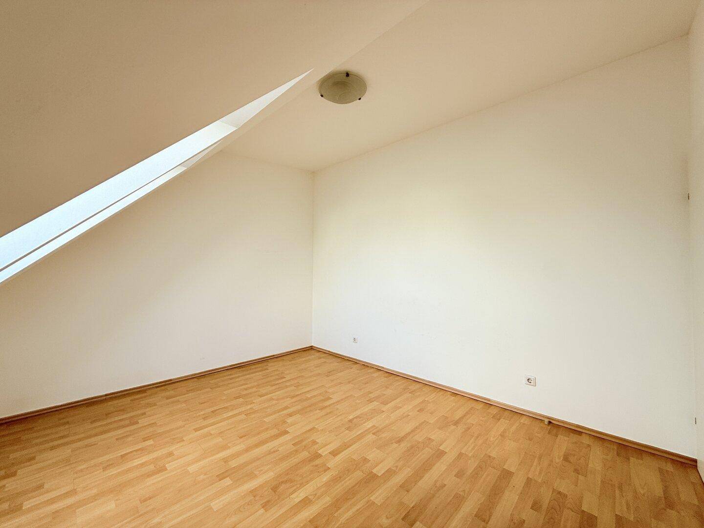 Kleineres Zimmer mit Dachschräge, einem Dachfenster und Parkettboden.