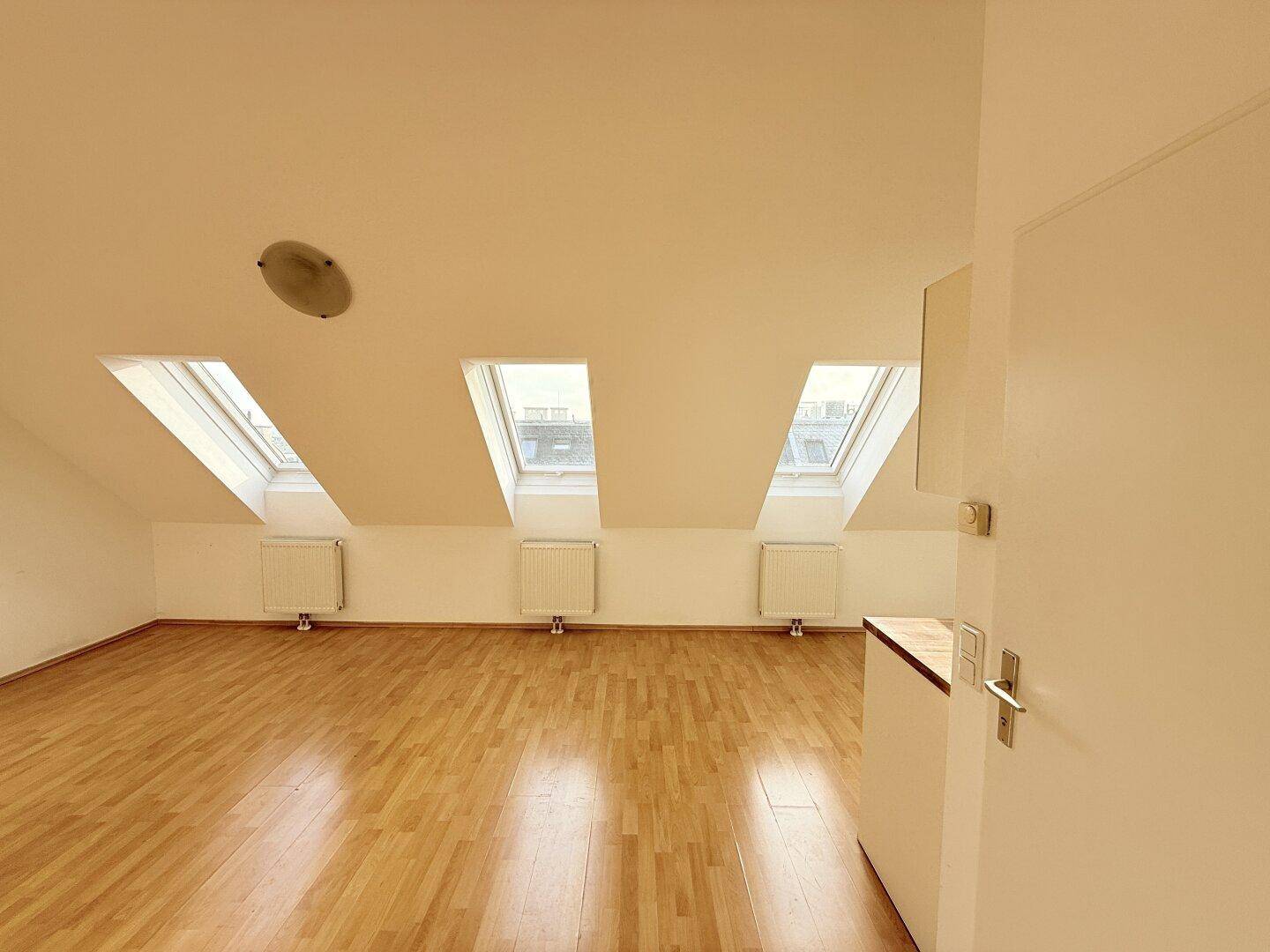 Geräumiger Wohnbereich im Dachgeschoss mit hellem Holzfußboden und Dachfenstern.