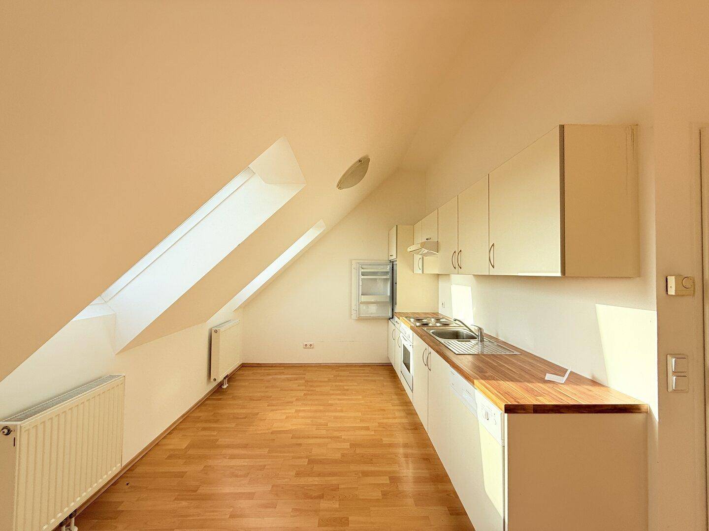 Kleine Küchenzeile mit Holz-Arbeitsplatte, Spüle und integrierten Geräten unter der Dachschräge.