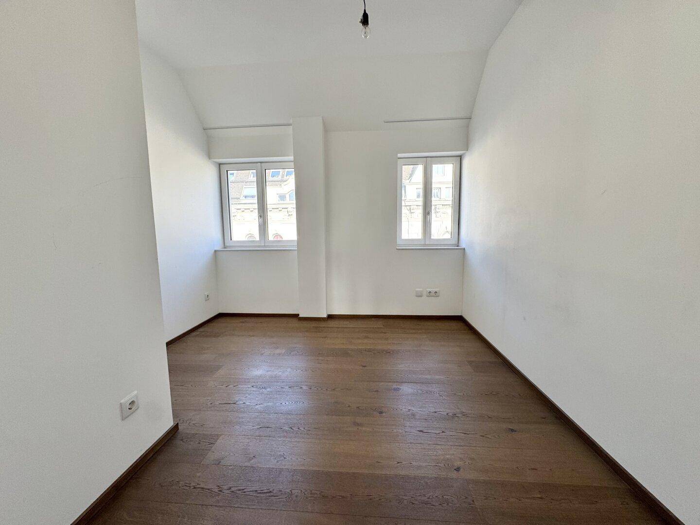 Helles Schlafzimmer mit Holzboden und zwei Fenstern, bereit zur individuellen Gestaltung.