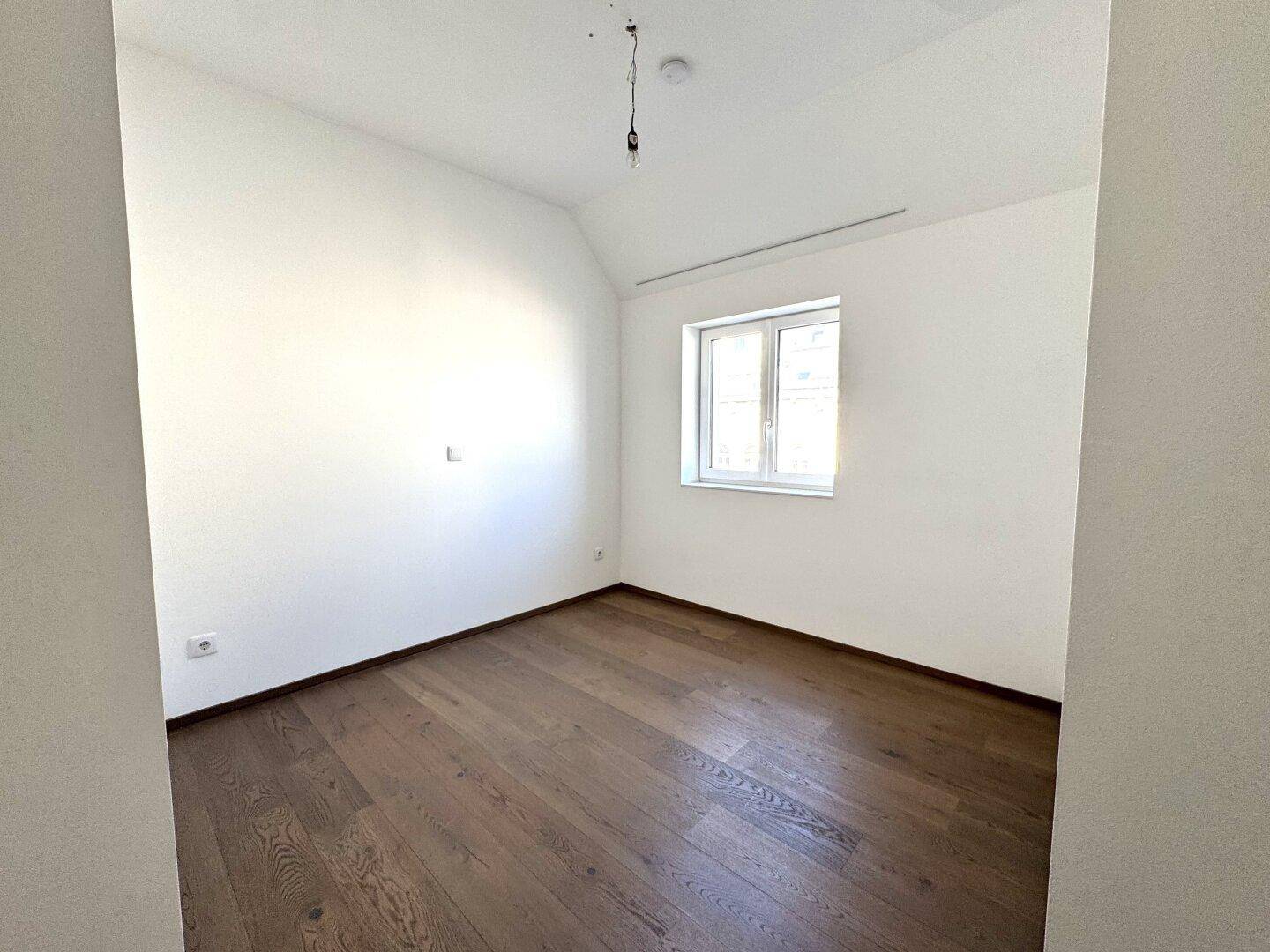 Ruhiges Schlafzimmer mit Holzboden und einem großen Fenster, ideal für erholsame Nächte.