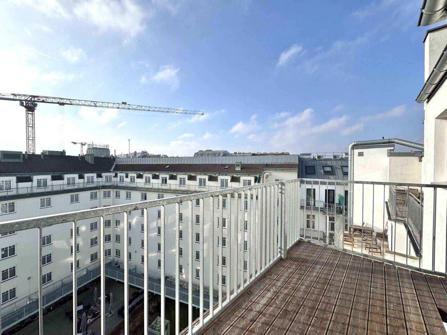 Balkon mit Holzboden und Blick auf den Innenhof eines modernen Gebäudekomplexes.