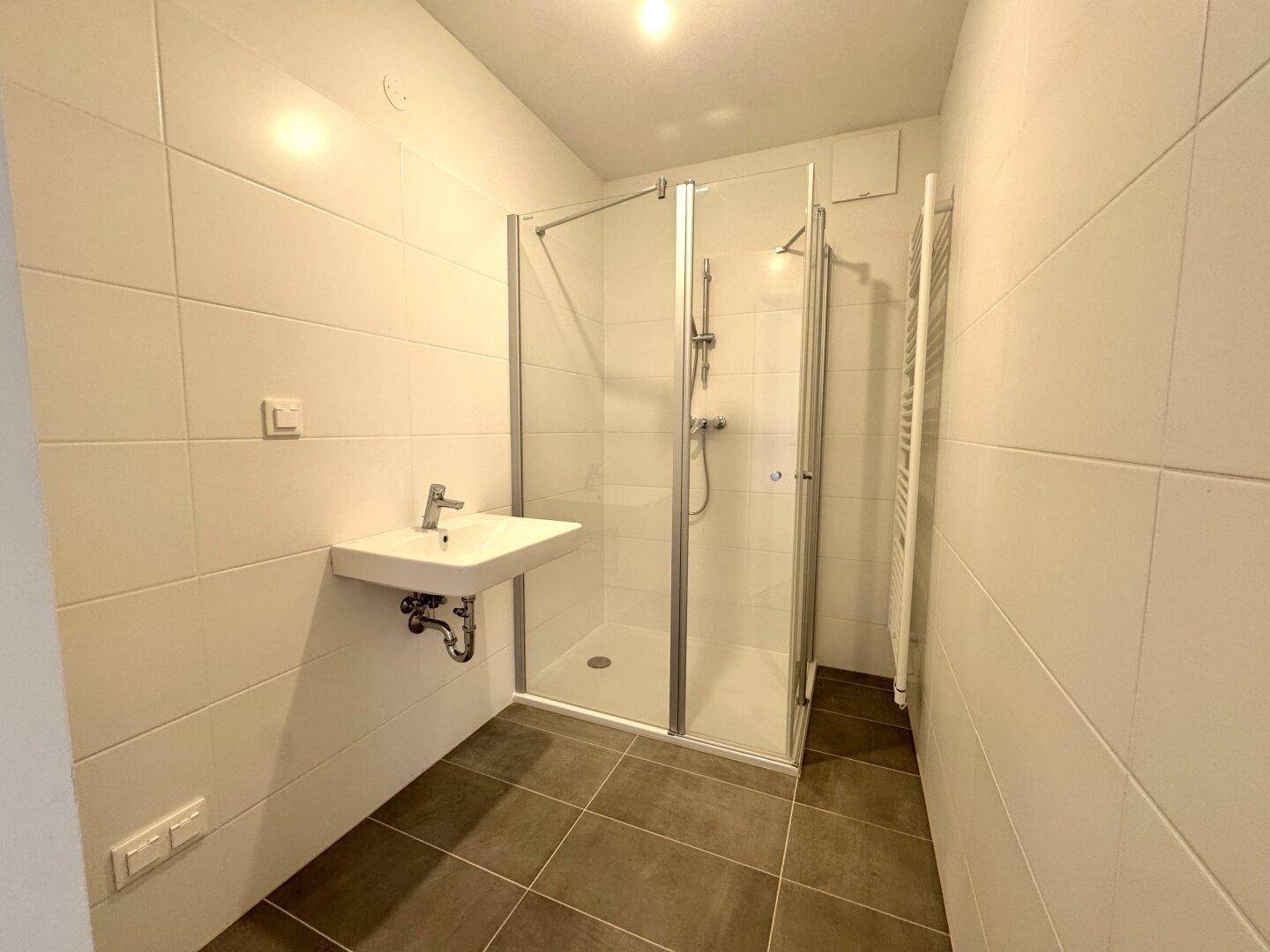 Modernes Badezimmer mit Duschkabine, Waschbecken und beheiztem Handtuchhalter.