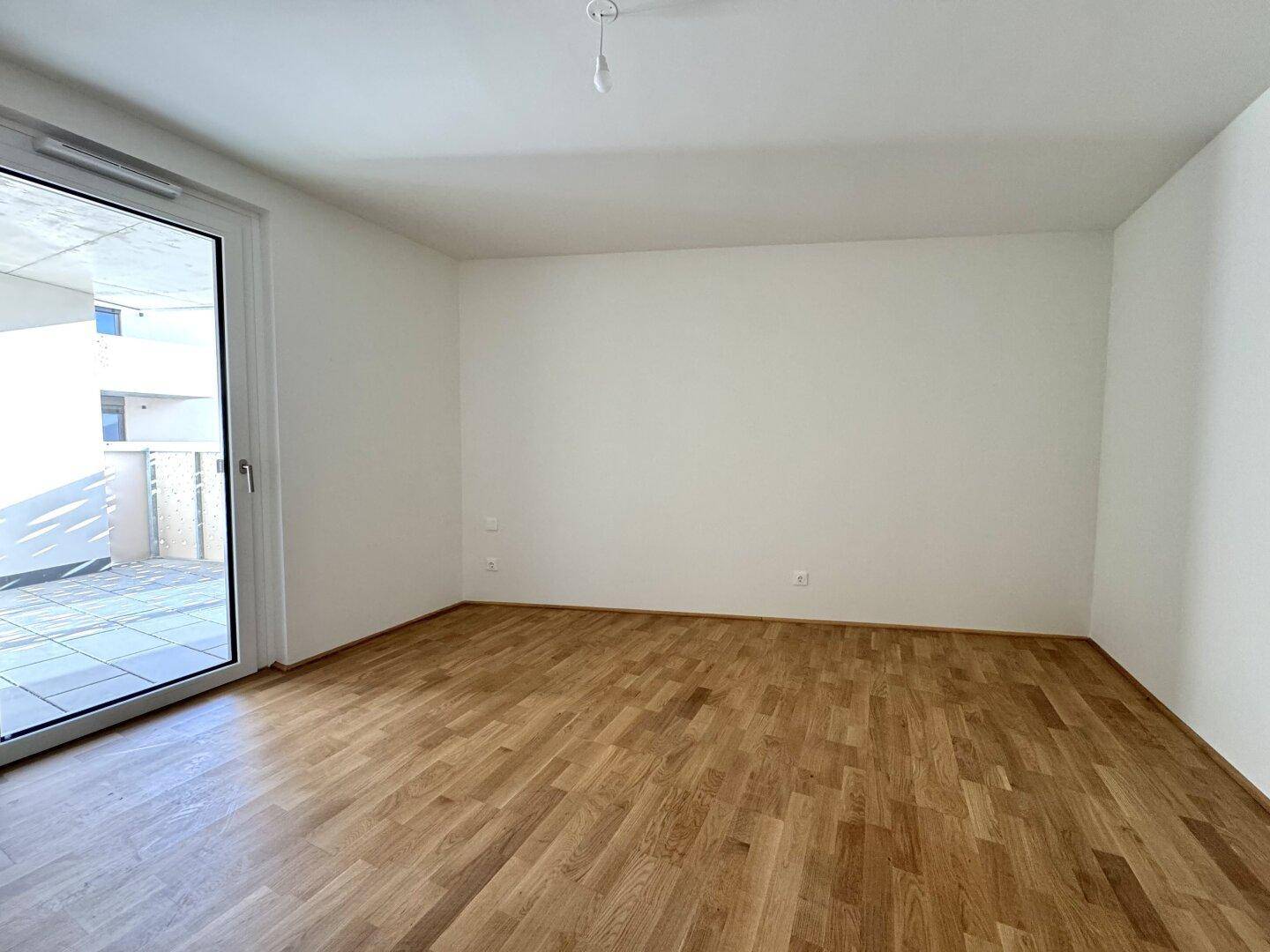 Heller Wohnraum mit Parkettboden und großer Fenstertür, die auf einen Außenbereich führt.