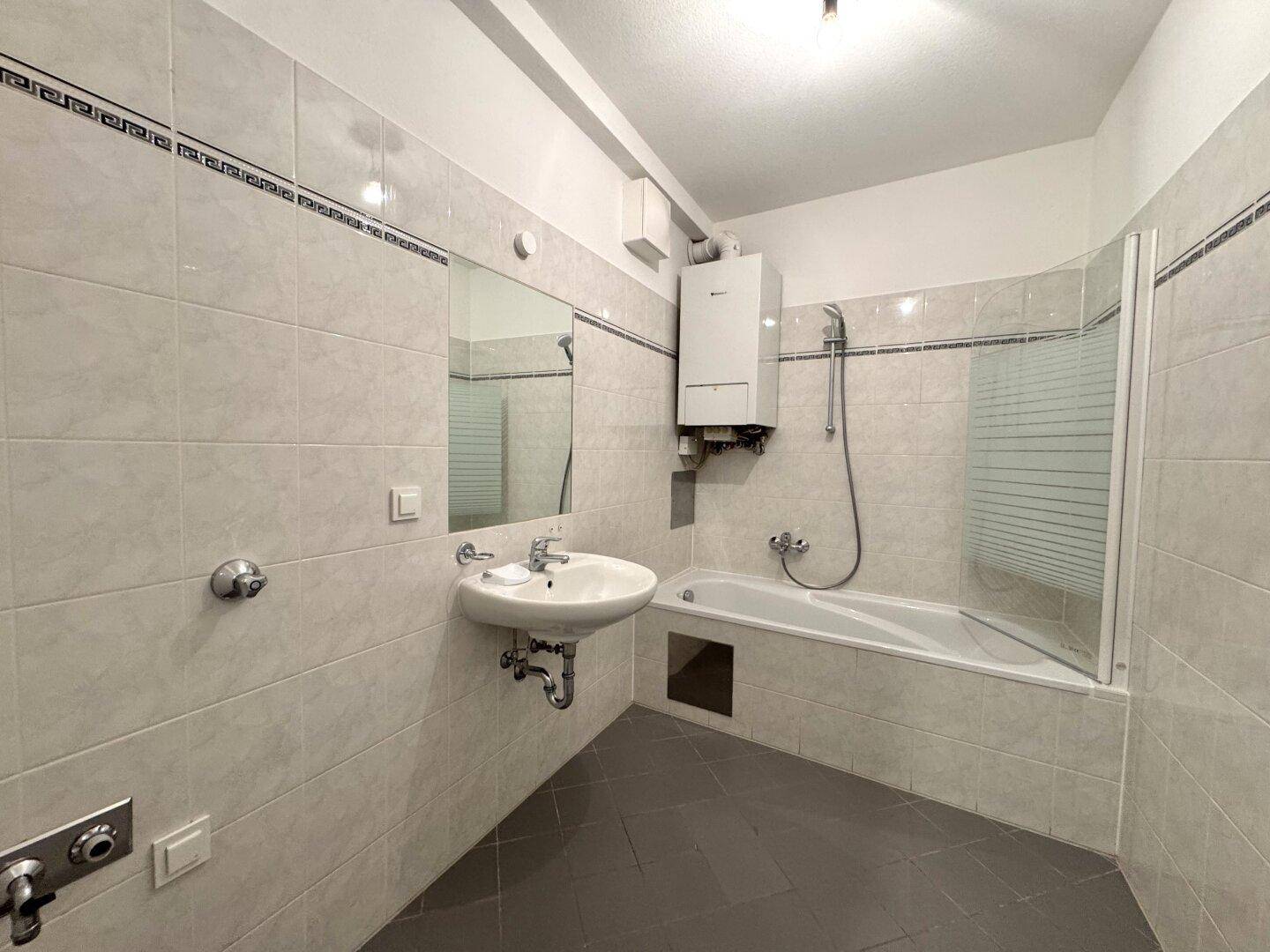 Gefliestes Badezimmer mit Badewanne, Duschfunktion und Waschbecken.