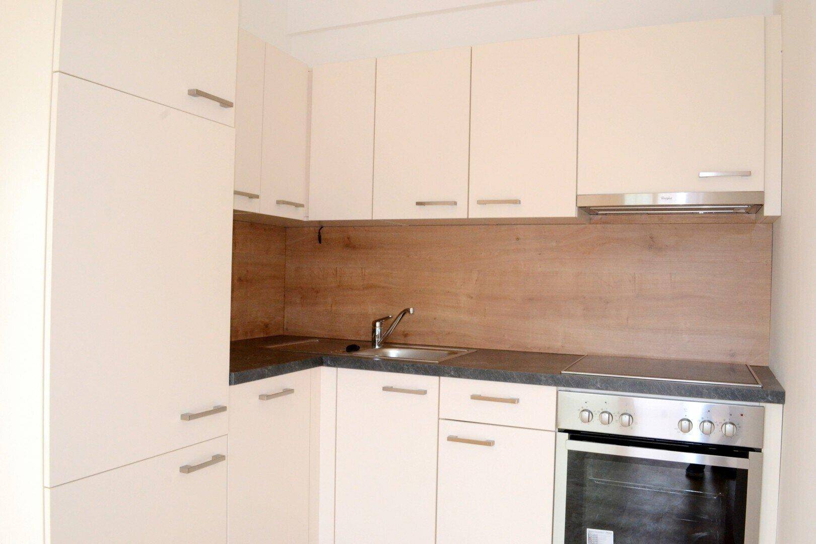 Kompakte Einbauküche in hellem Beige mit modernen Geräten und dunkler Arbeitsplatte.
