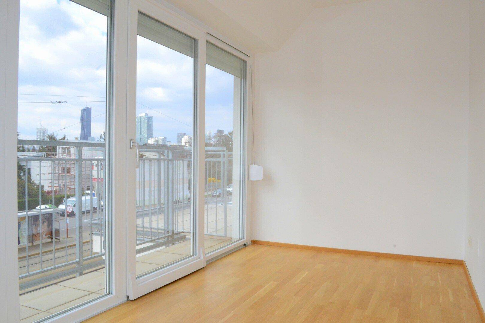 Heller Raum mit Parkettboden und großen Schiebetüren, die zu einem Balkon mit Stadtblick führen.