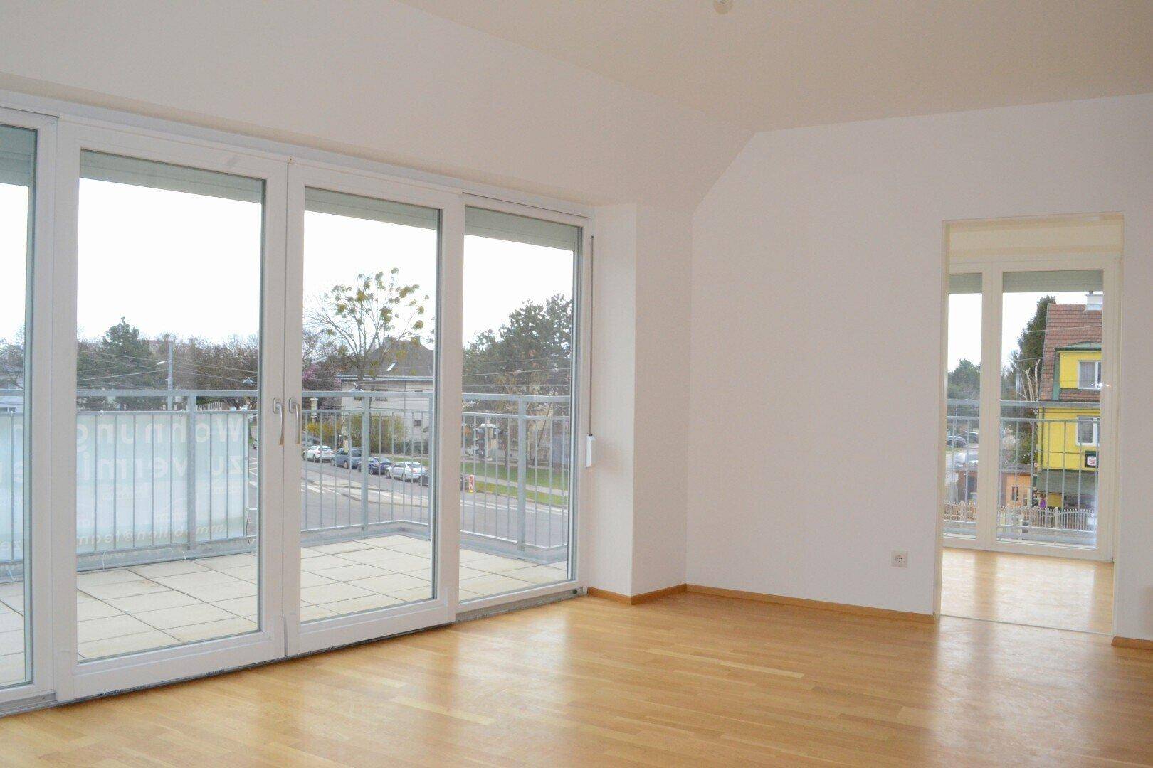 Geräumiger, heller Raum mit Parkettboden und Zugang zu einem Balkon mit Blick auf die Umgebung.