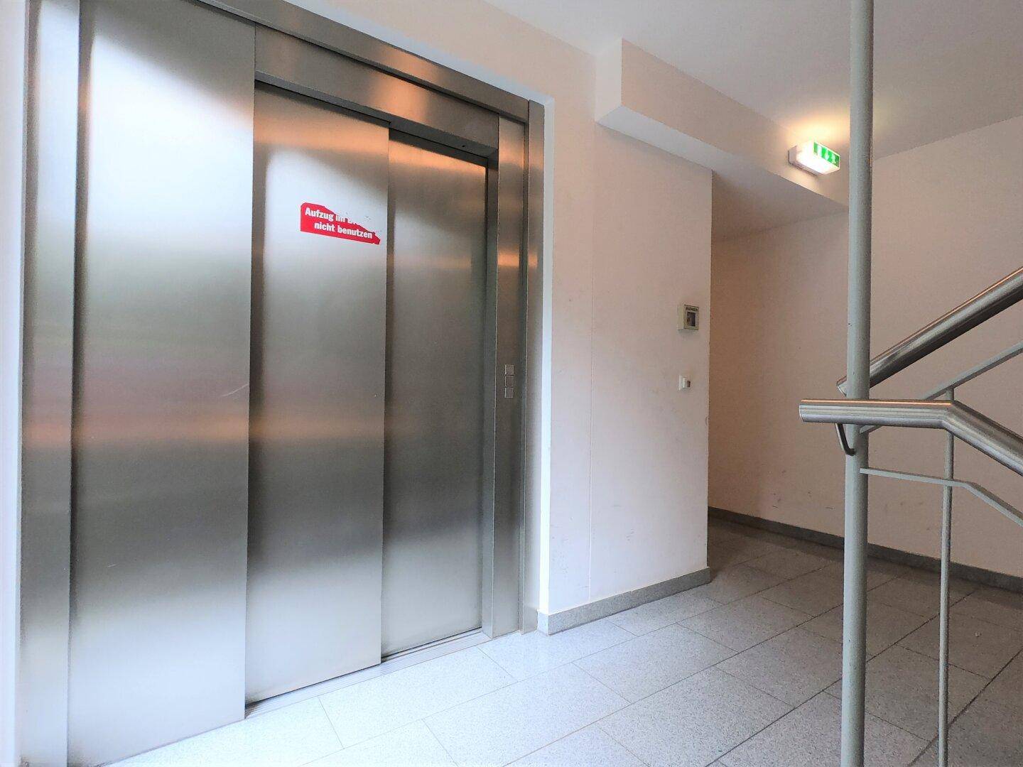 Moderner Aufzug mit Edelstahltüren und Fliesenboden im Eingangsbereich des Gebäudes.