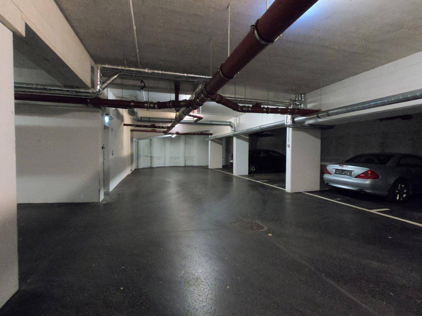 Geräumige Tiefgarage mit Betonboden und sichtbaren Leitungen, bietet Stellplätze für Fahrzeuge.