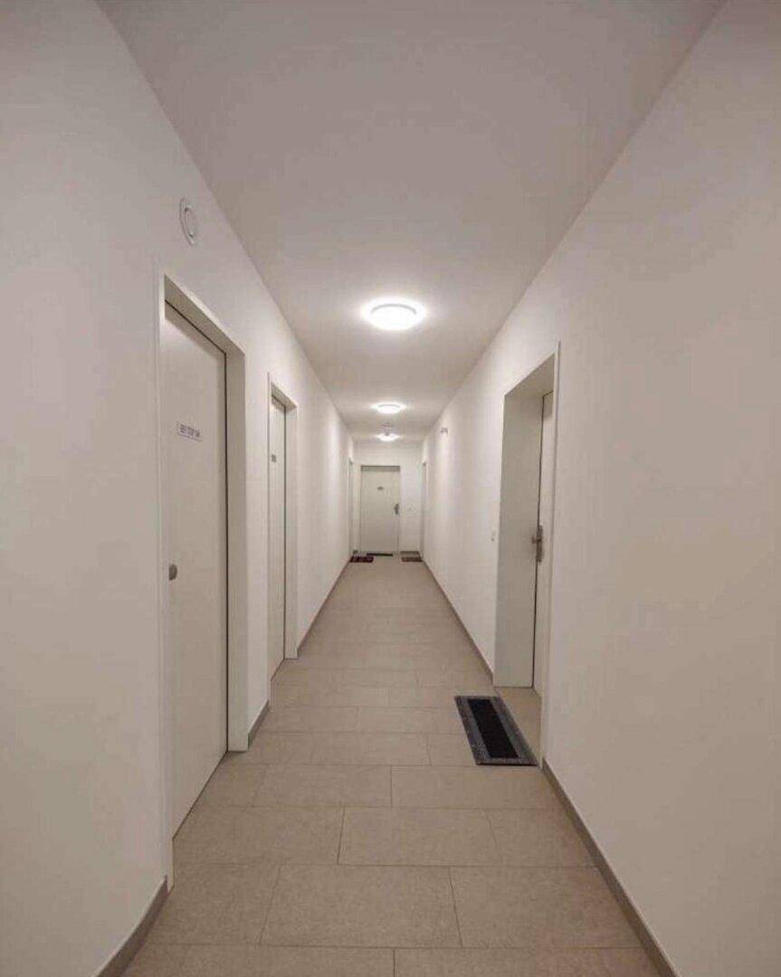 Langer, sauberer Flur mit Fliesenboden und mehreren Türen in einem Mehrfamilienhaus.