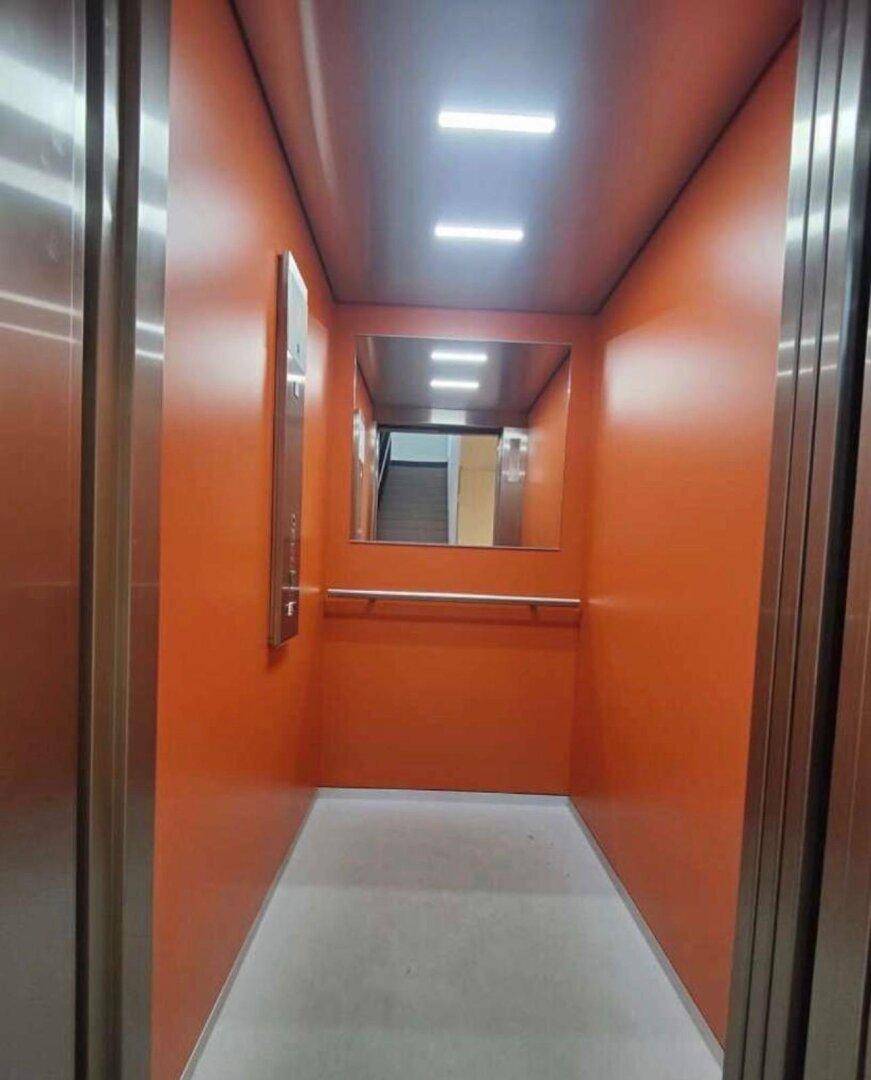 Moderner Aufzug mit orangefarbenen Wänden und einem Spiegel im Inneren des Gebäudes.