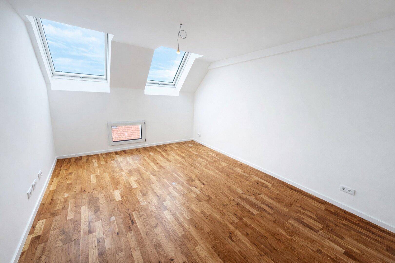 Heller Raum im Dachgeschoss mit Holzboden und zwei Dachfenstern, ideal für Schlaf- oder Arbeitszimmer.