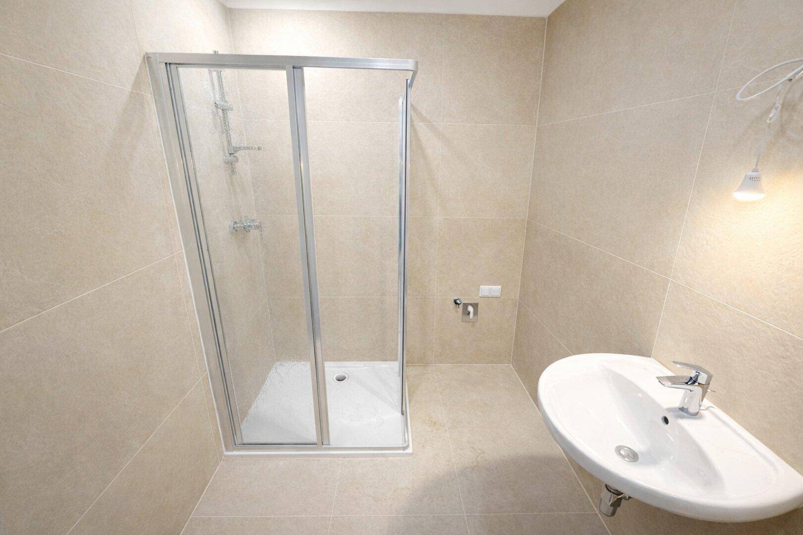 Modernes Badezimmer mit beigefarbenen Fliesen, Duschkabine und einem einzelnen Waschbecken.