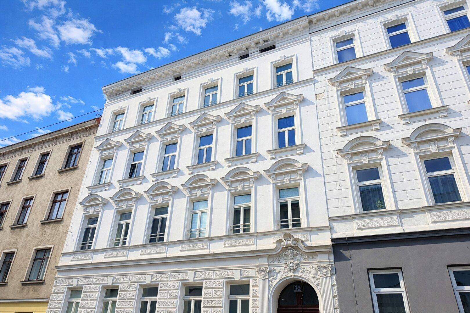 Historische weiße Fassade eines Gebäudes mit vielen Fenstern und architektonischen Details.