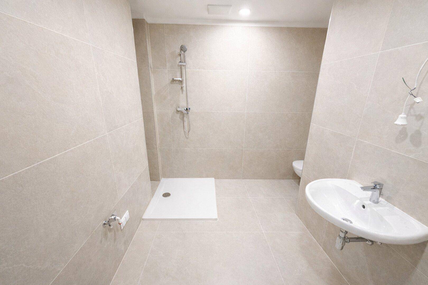 Modernes Badezimmer mit beigefarbenen Fliesen, Dusche und wandmontiertem Waschbecken.