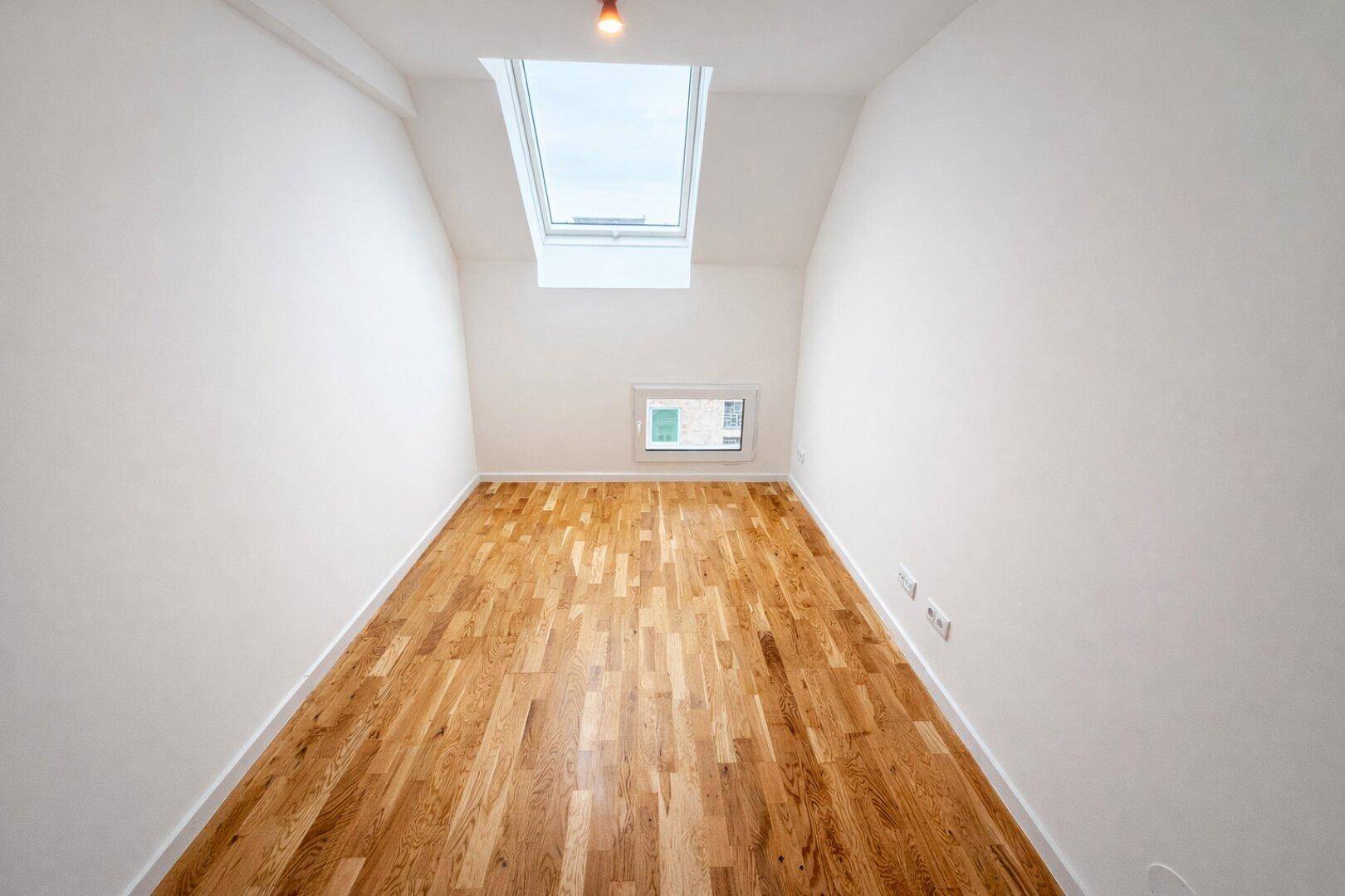 Gemütliches Schlafzimmer im Dachgeschoss mit einem Dachfenster und Holzboden.