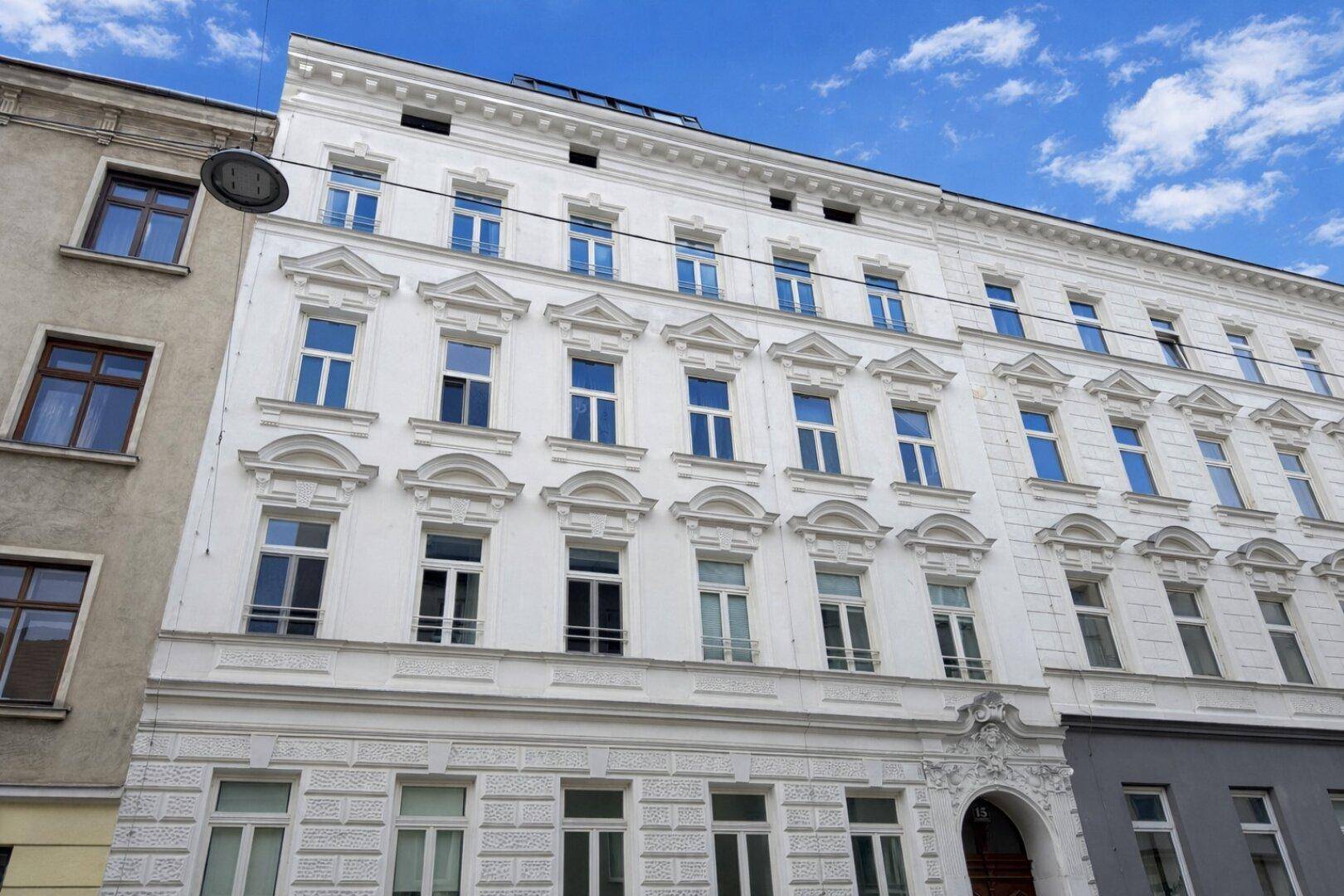 Weiße Fassade eines renovierten Altbaus mit vielen Fenstern und klassischer Architektur.