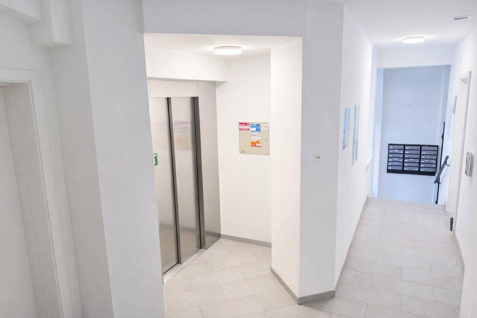 Heller Flur im Gebäude mit Aufzug und Briefkästen, modern gefliest.