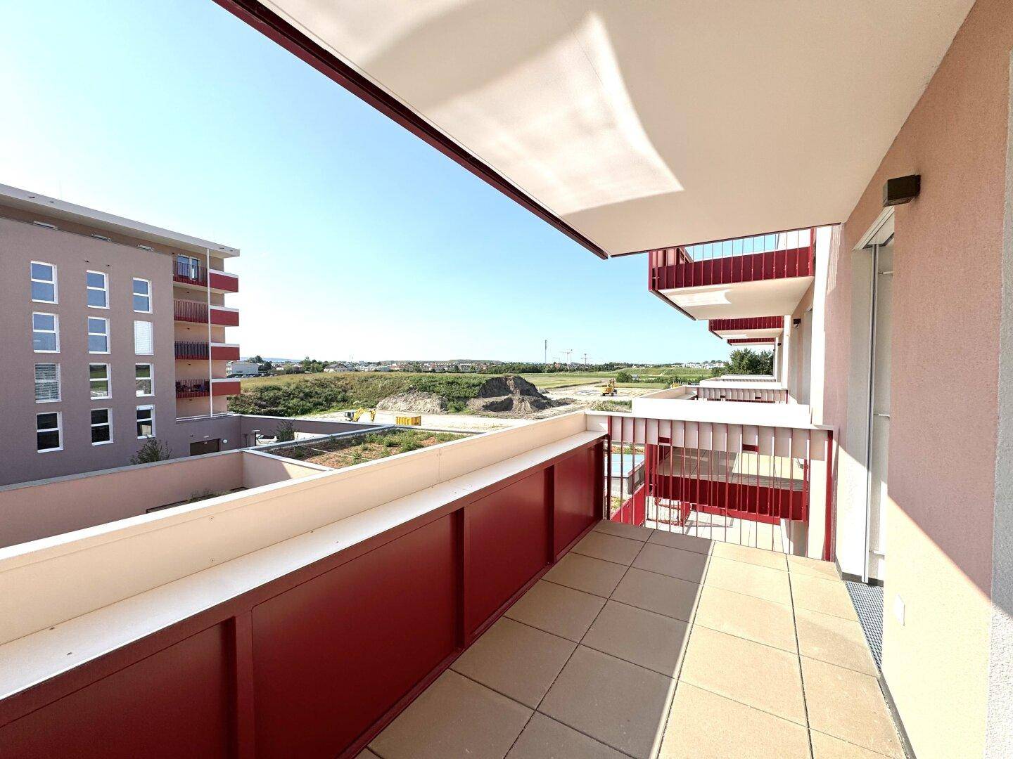 Geräumiger Balkon mit Fliesenboden und rotem Geländer, bietet Blick auf die umliegende Landschaft.