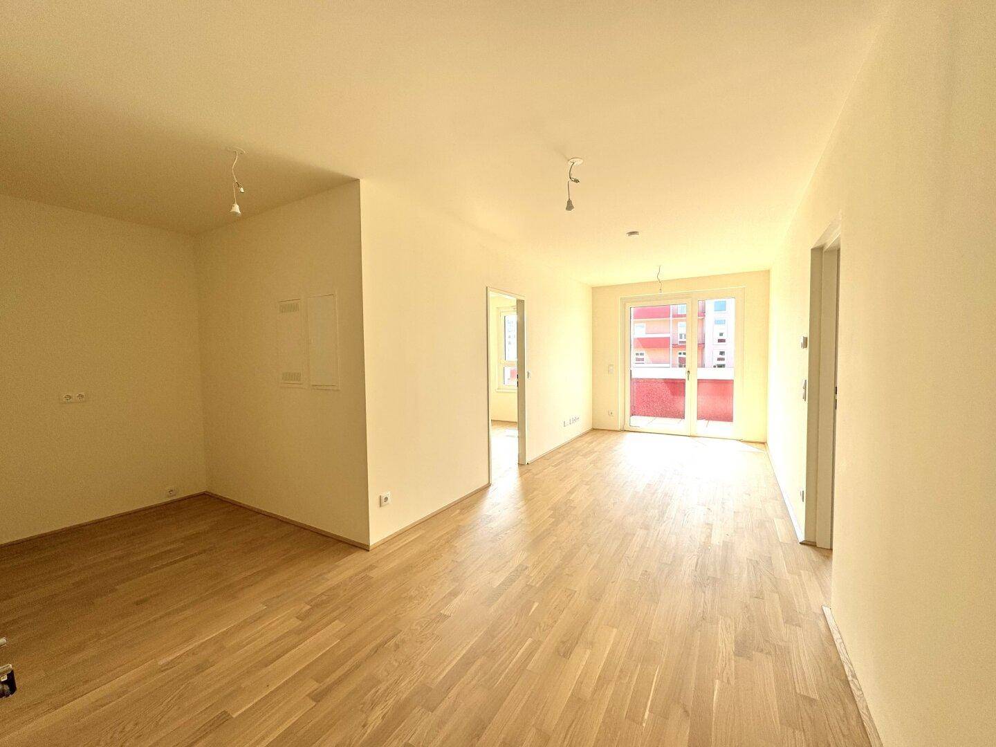 Heller, leerer Raum mit Parkettboden und Zugang zu einem Balkon.