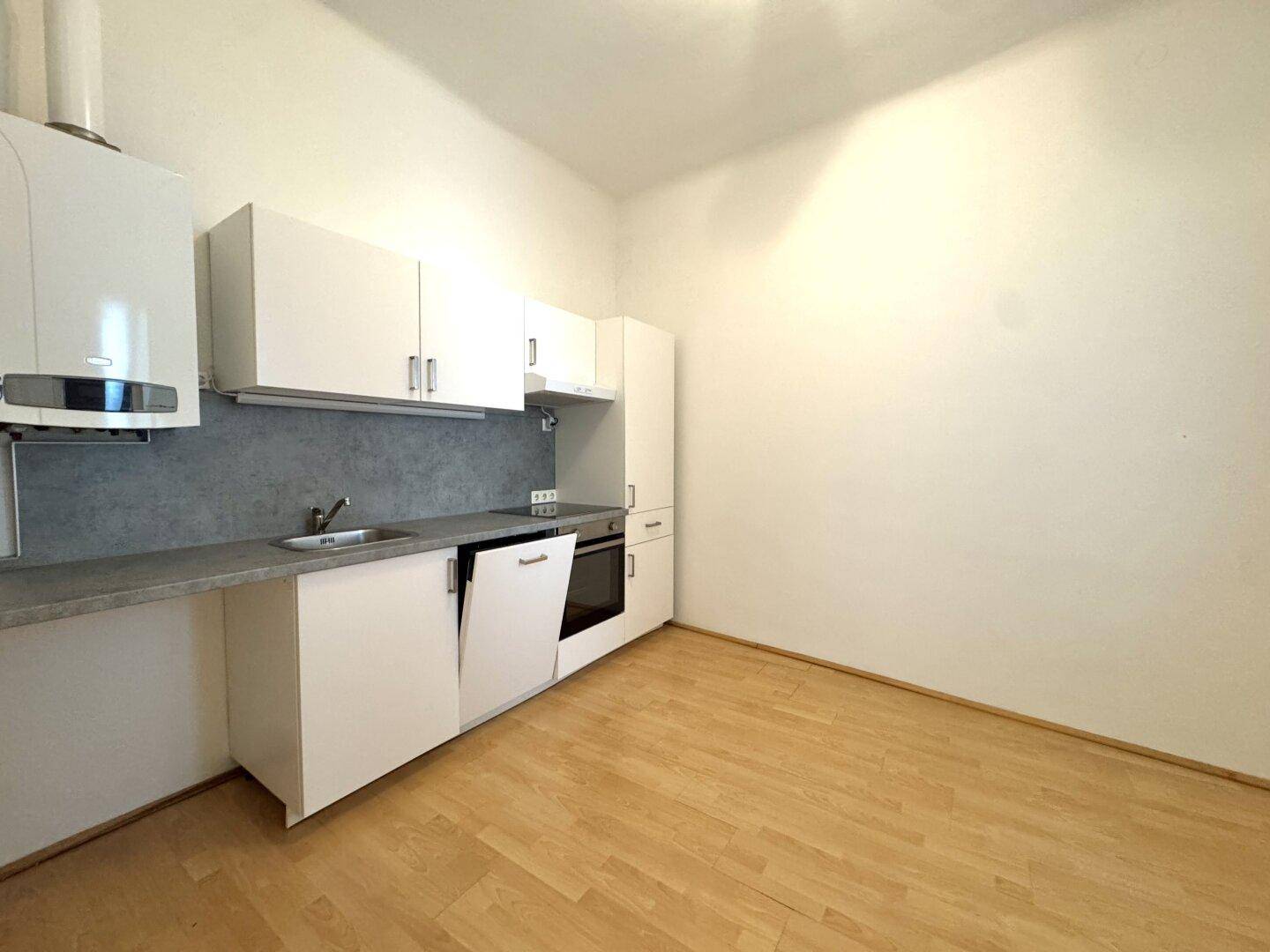 Kleine, funktionale Küche mit weißen Schränken, Spüle und integrierten Geräten, inklusive Gastherme.