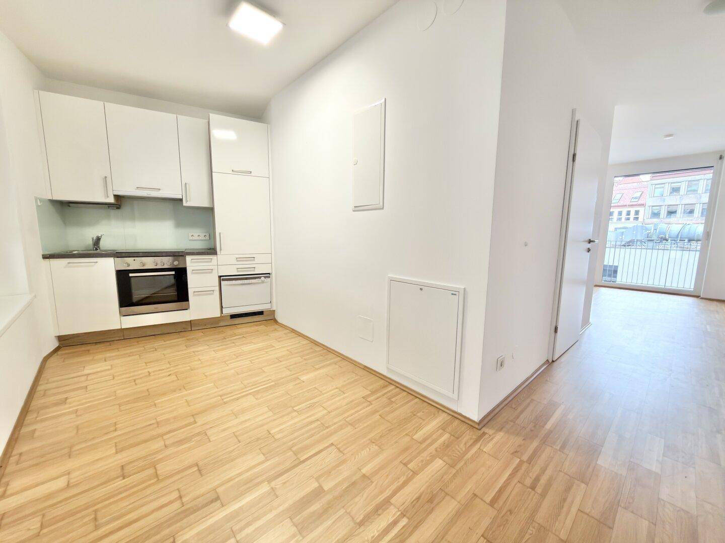Moderne Einbauküche mit weißen Schränken, integrierten Geräten und Parkettboden.