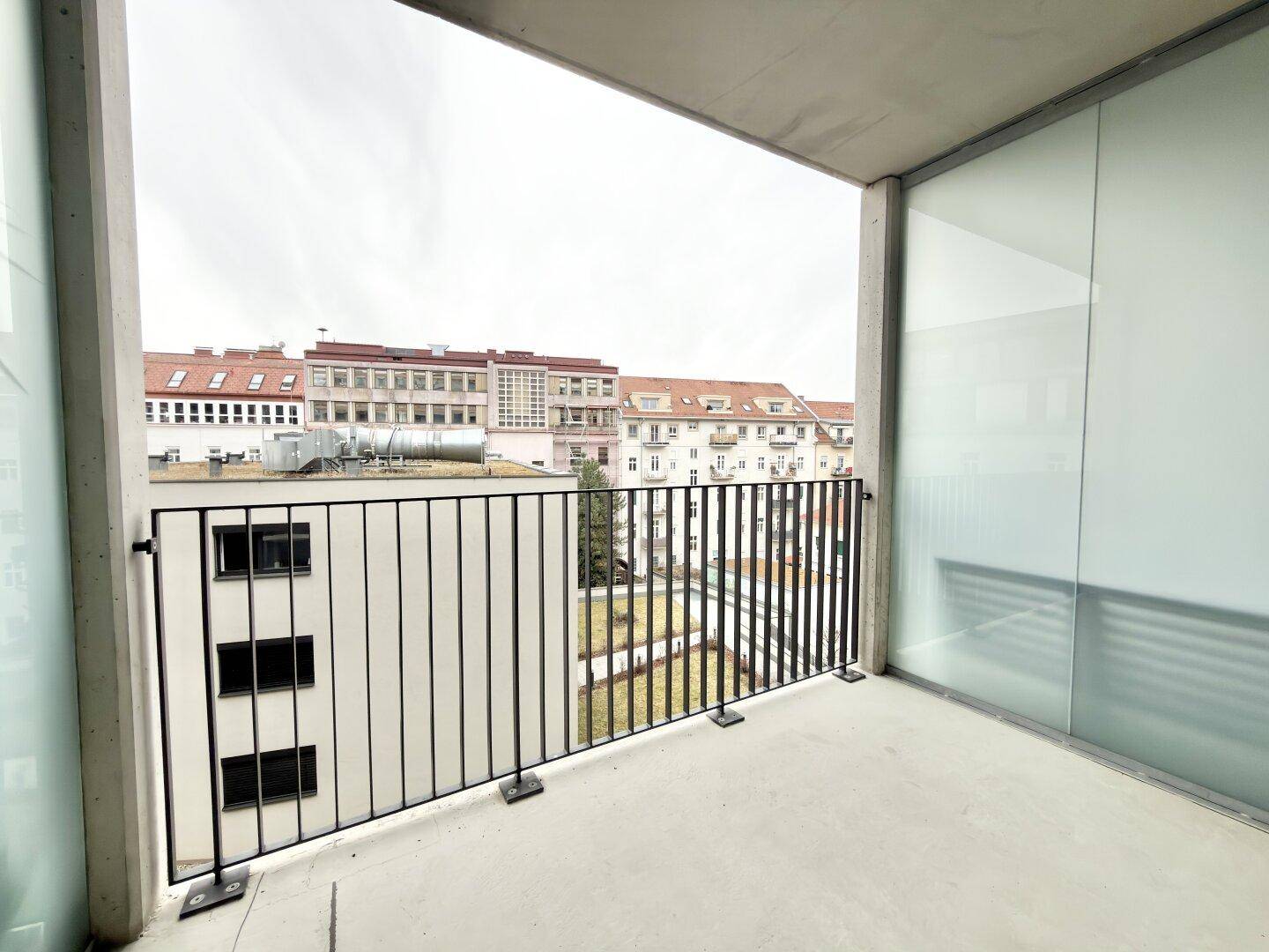 Balkon mit Blick auf die umliegenden Gebäude und einen begrünten Innenhof.