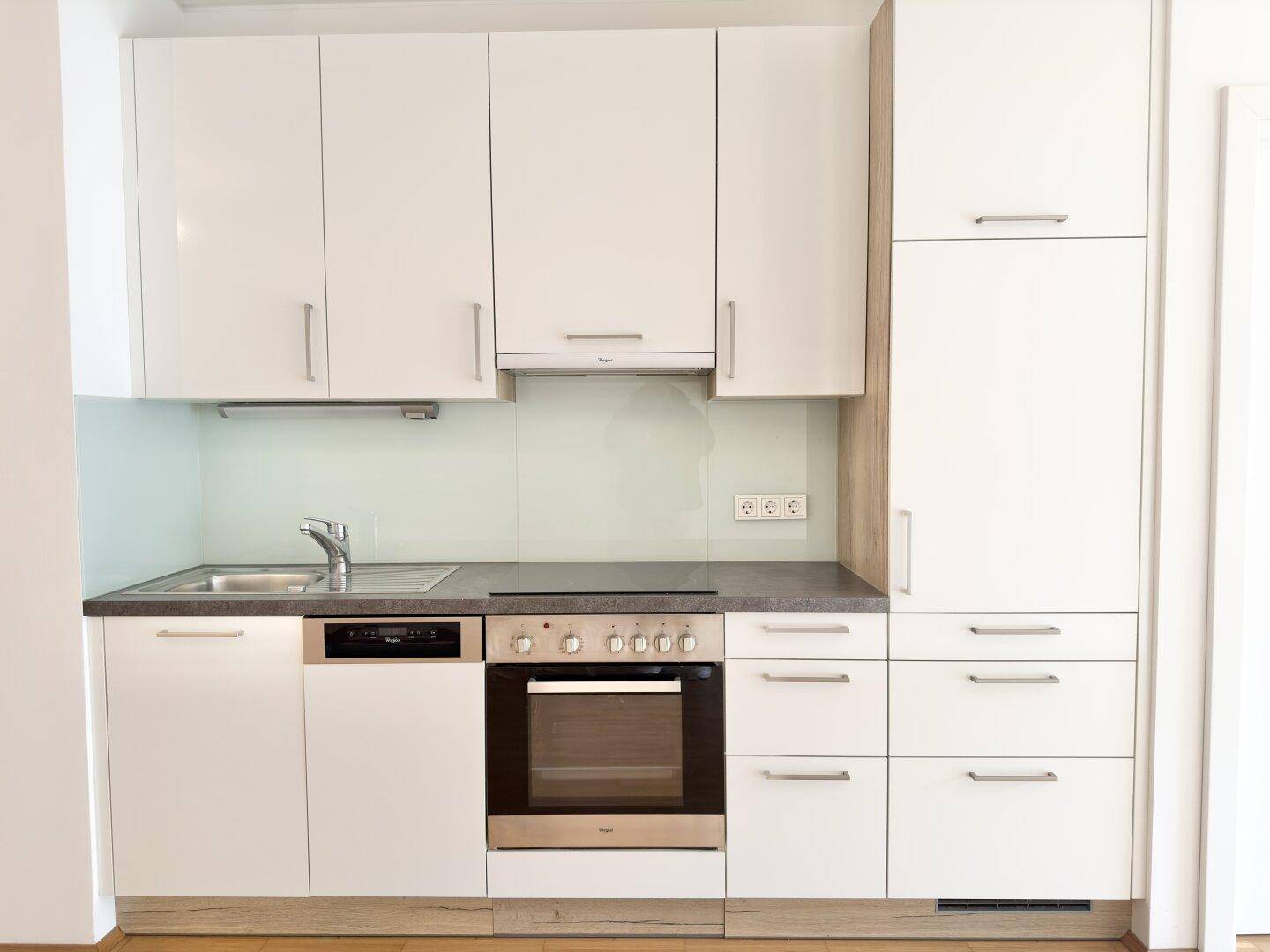 Moderne Einbauküche in Weiß mit integrierten Geräten und dunkler Arbeitsplatte.