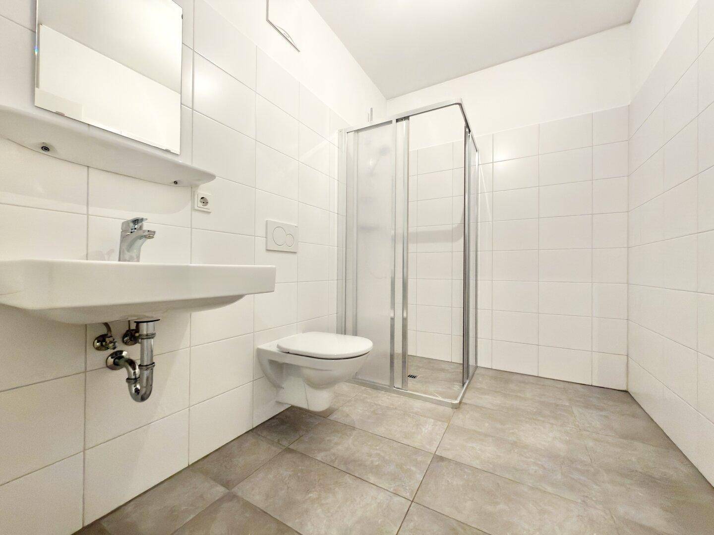 Modernes Badezimmer mit weißen Fliesen, Duschkabine, WC und Waschbecken.