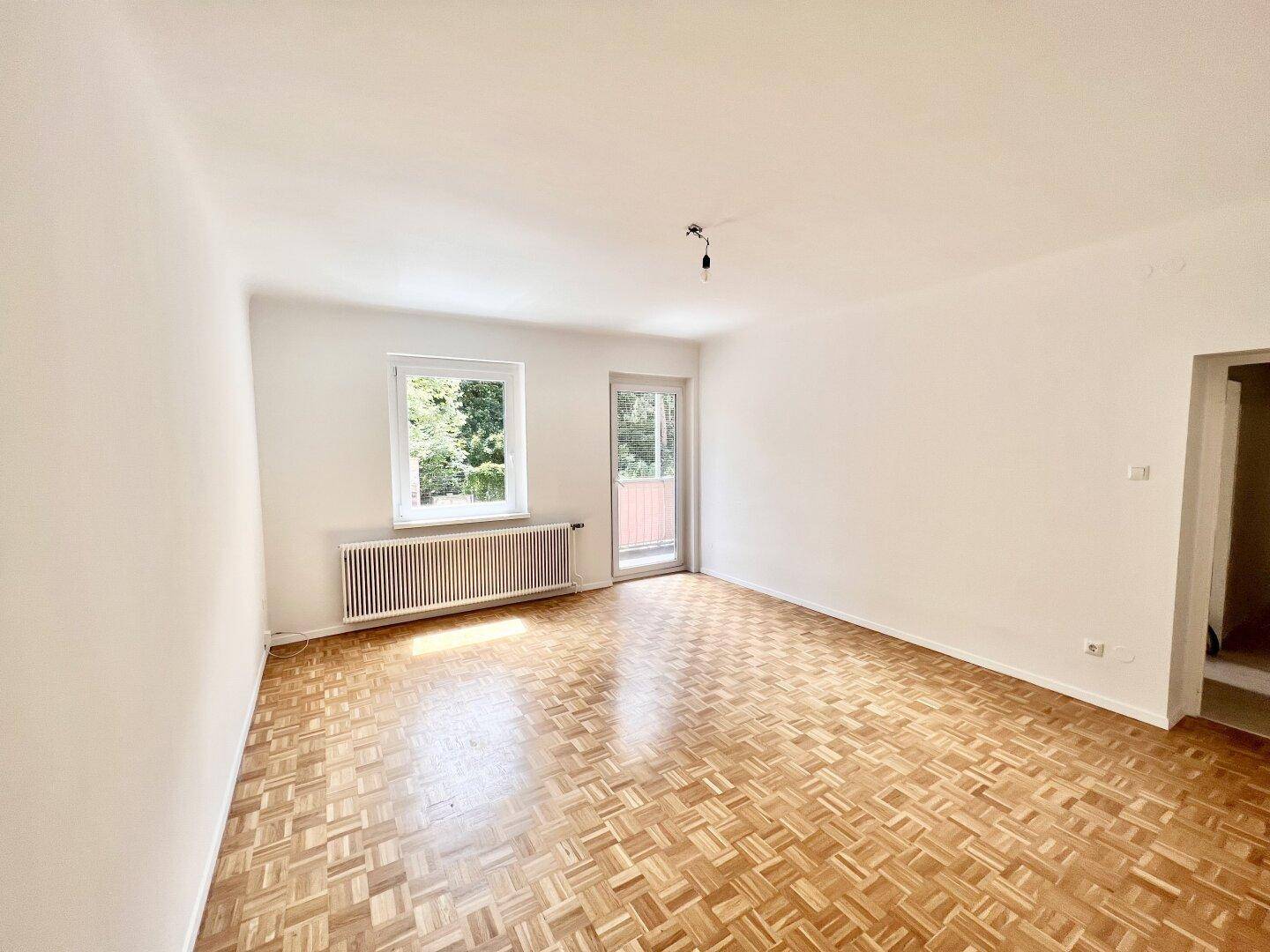 Leeres Wohnzimmer mit Parkettboden, Fenster und Balkonzugang, bereit zur Gestaltung.
