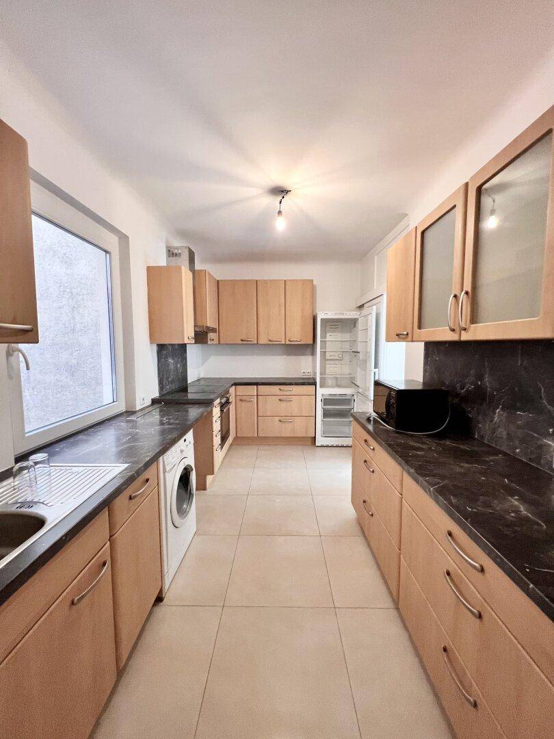 Geräumige Küche mit Holzschränken, Fliesenboden und dunklen Arbeitsplatten.