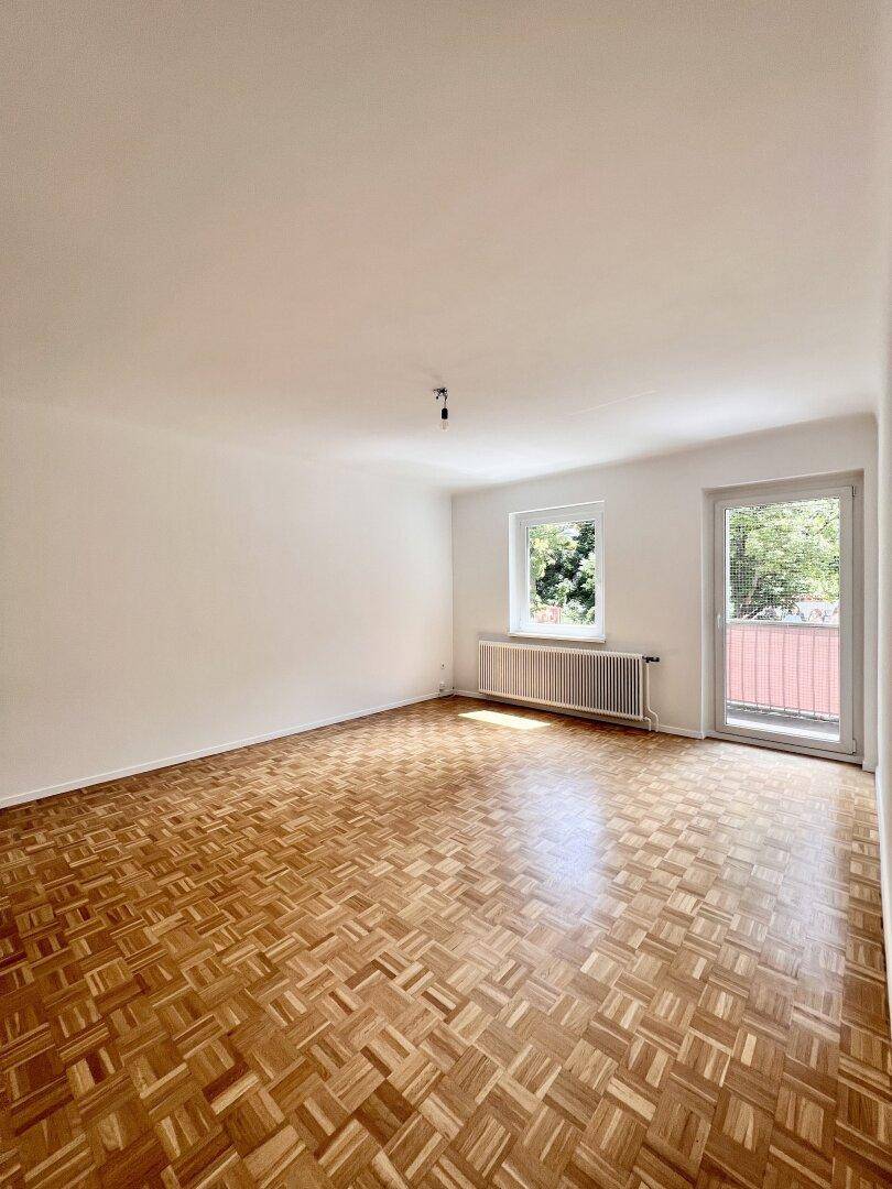 Leeres Wohnzimmer mit Parkettboden, Fenster und Balkonzugang, bereit zur Gestaltung.