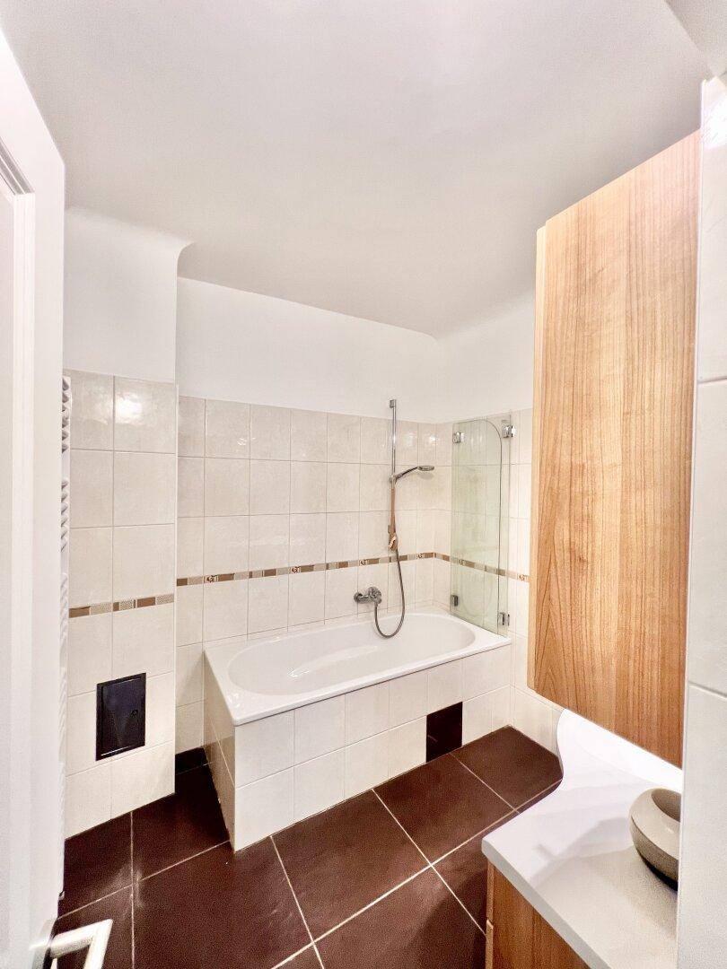 Helles Badezimmer mit Badewanne, Duschabtrennung und braunen Bodenfliesen.