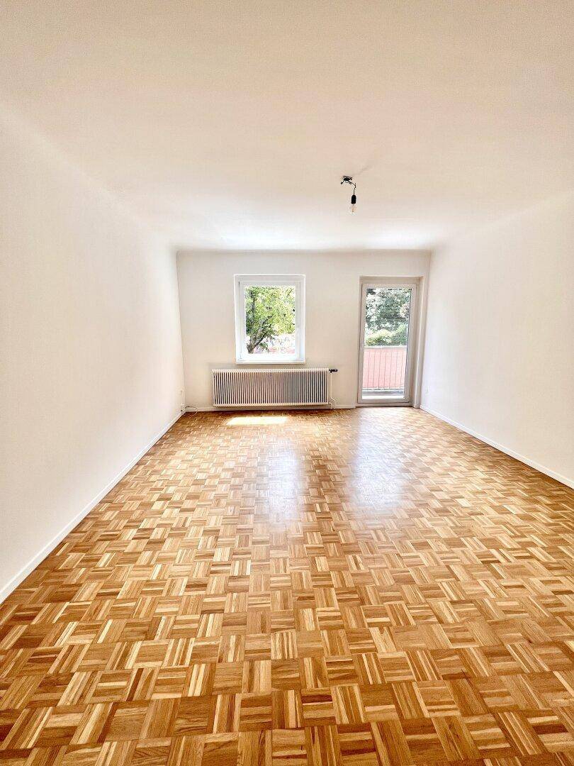 Leeres Wohnzimmer mit hellem Parkettboden und Zugang zu einem Außenbereich.