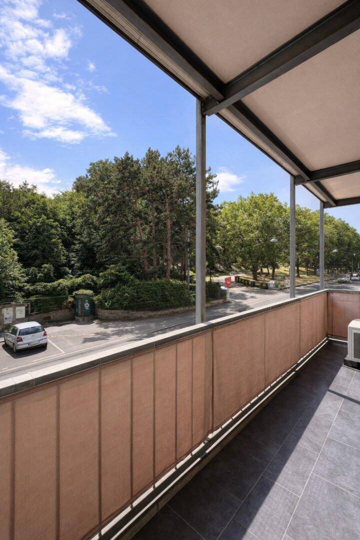 Balkon mit Blick auf grüne Bäume und die umliegende Straße.