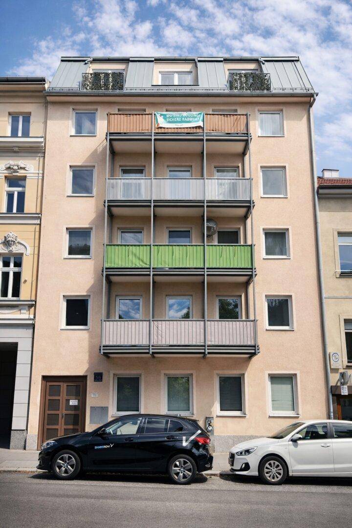 Mehrstöckiges Wohngebäude mit mehreren Balkonen und Mansarddach in städtischer Umgebung.