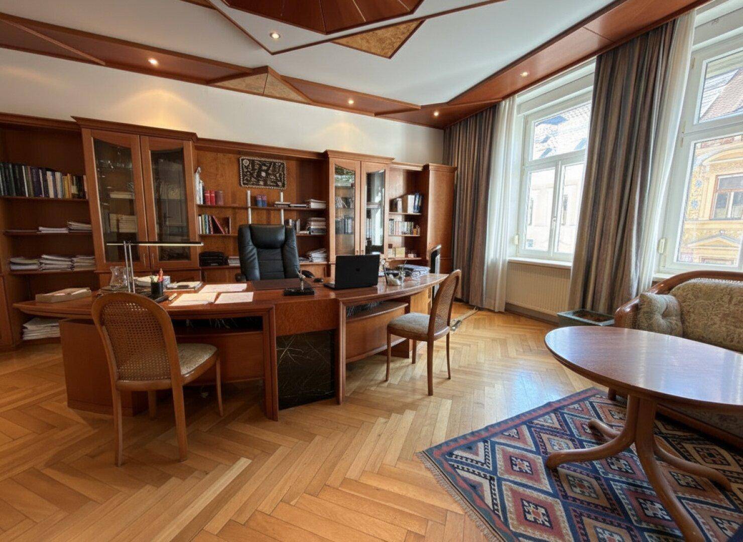 Elegantes Büro mit Holzmöbeln, Fischgrätparkett und einer dekorativen Holzdecke.