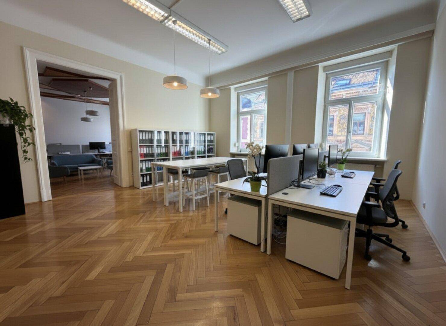 Modern eingerichtetes Großraumbüro mit mehreren Arbeitsplätzen und Fischgrätparkett.