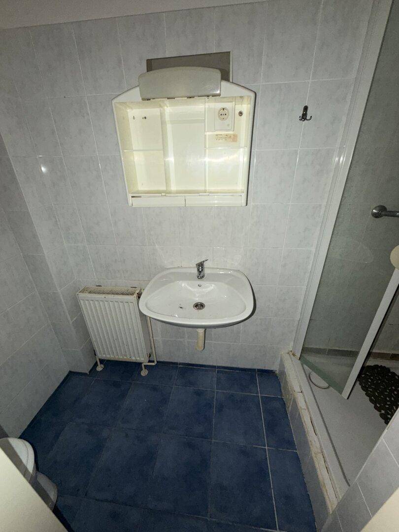 Badezimmer mit blauen Bodenfliesen, Waschbecken, Spiegelschrank und Heizkörper.