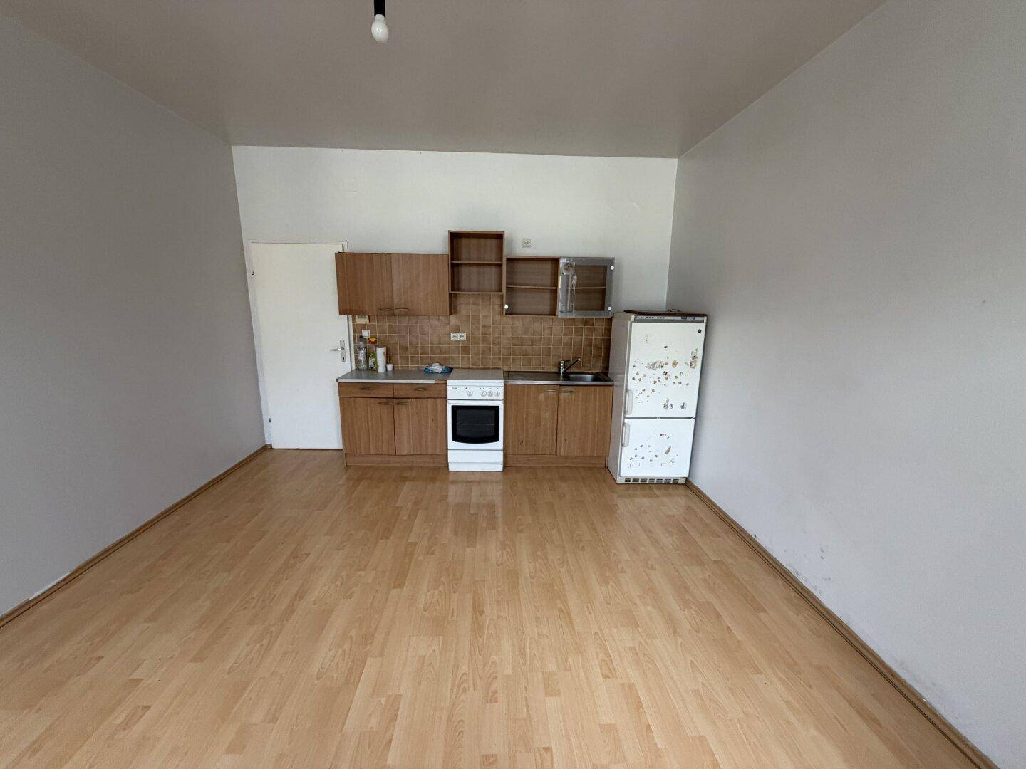 Einfache Küche mit älteren Holzschränken, Herd und Kühlschrank, bereit für eine Modernisierung.