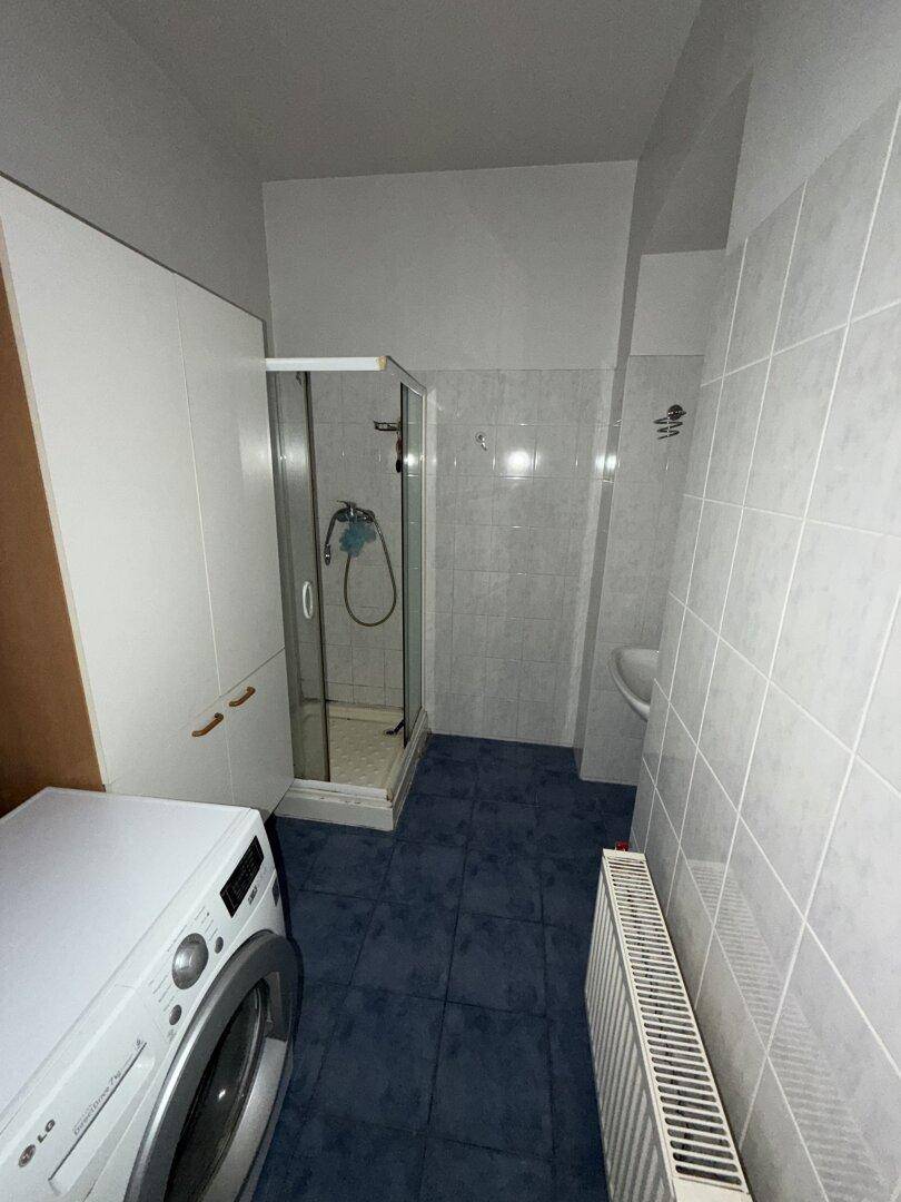 Badezimmer mit Duschkabine, Waschmaschine und hellgrauen Fliesen, funktional und sauber.