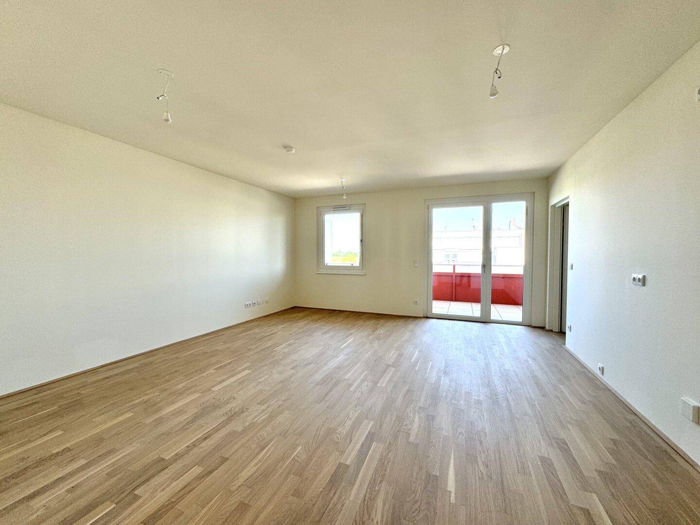 Helles Wohnzimmer mit Parkettboden und Zugang zu einem Balkon.